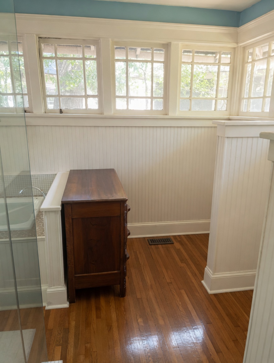 The master bath with clerestory windows wrapping the corner above white beadboard wainscot.